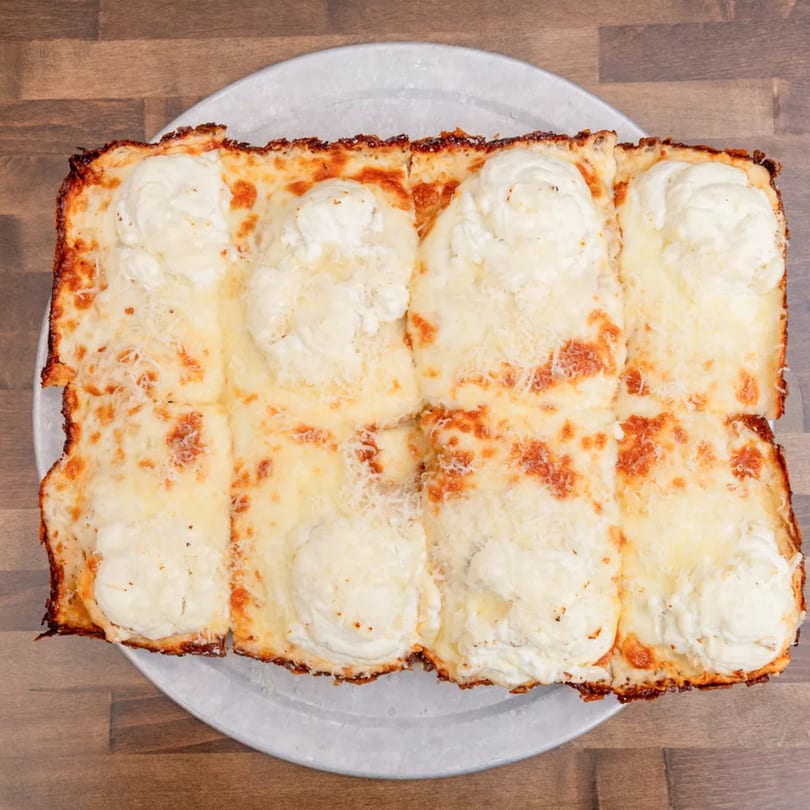 Overhead view of a rectangular white pizza with dollops of ricotta cheese, cut into eight squares.