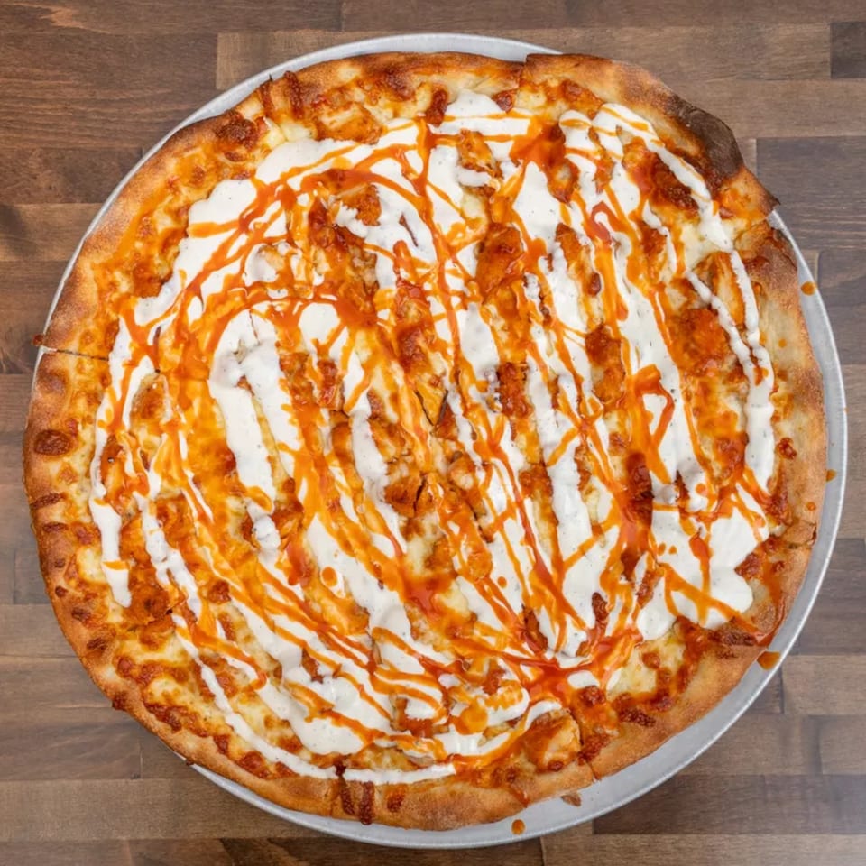 Overhead view of a buffalo chicken pizza with ranch and hot sauce drizzle on a wooden table.