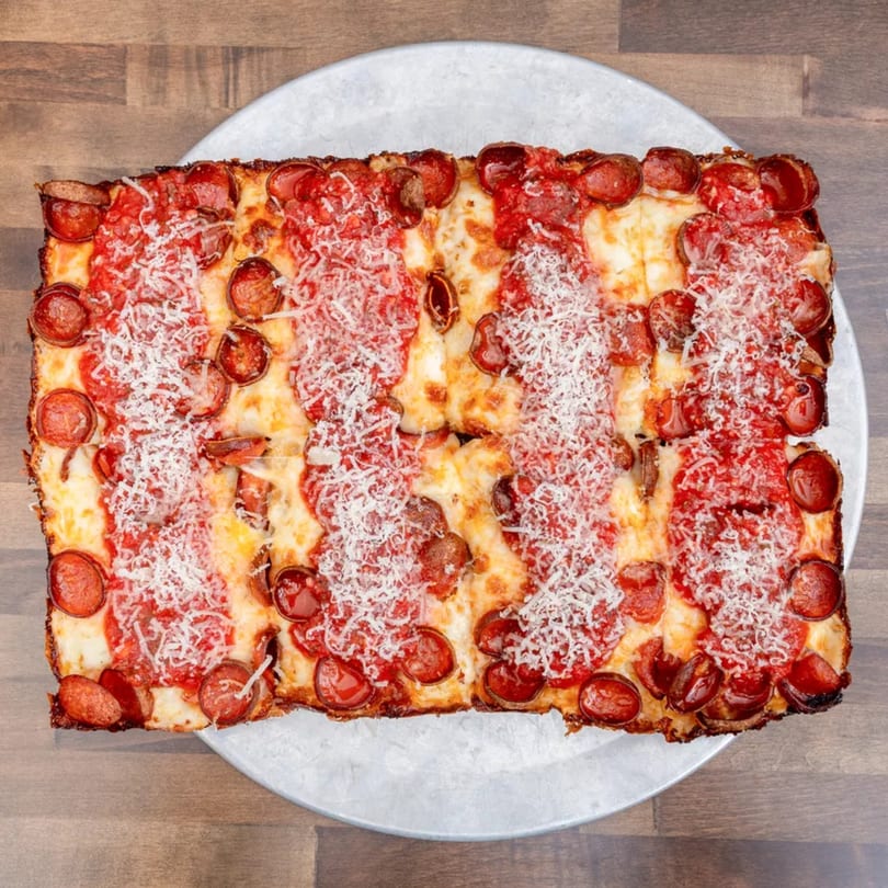 Rectangular Detroit-style pepperoni pizza with red sauce stripes and grated cheese on a metal pan.