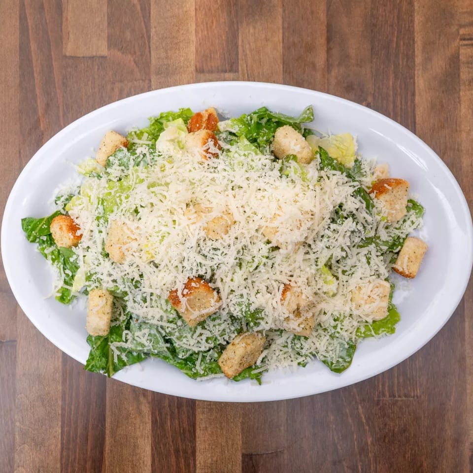 A Caesar salad with romaine lettuce, croutons, and grated Parmesan cheese on a white oval plate.