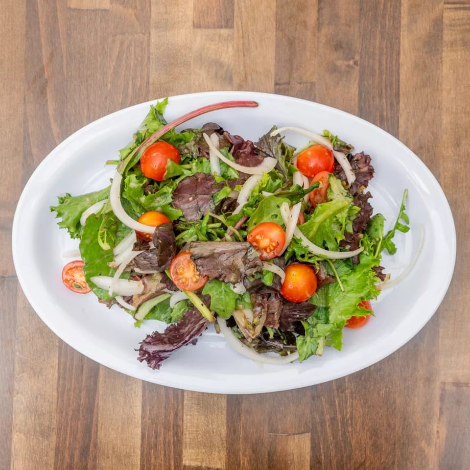 Fresh garden salad with mixed greens, cherry tomatoes, and sliced onions on a white oval plate.