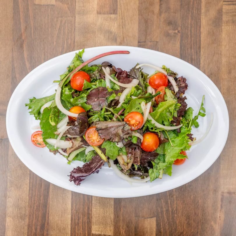 Fresh garden salad with mixed greens, cherry tomatoes, and sliced onions on a white oval plate.